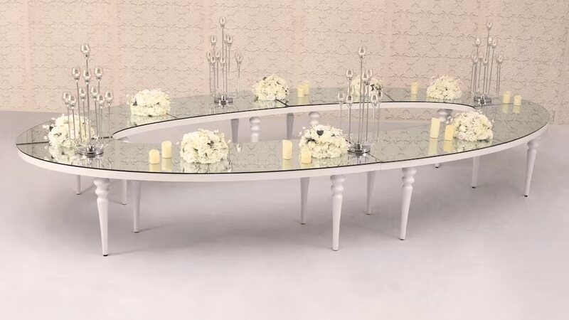 Large white oval table with mirror top and turned white legs, dressed with white floral arrangements, candelabras and candles