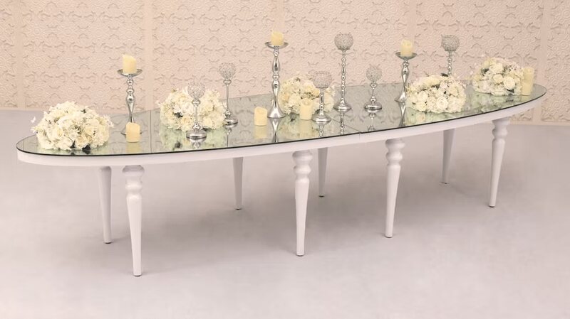 Long oval table with mirror top and white bubble legs, styled with white floral arrangements, silver candlesticks and candles