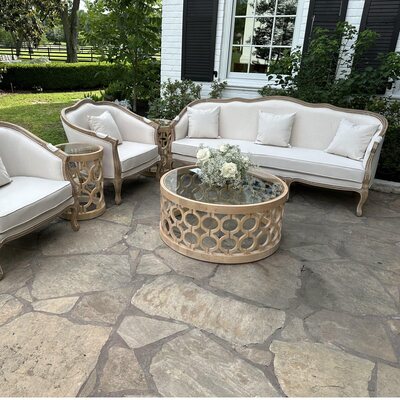 Off-white sofa, two armchairs and lattice coffee table arranged on a flagstone patio outside a white brick house