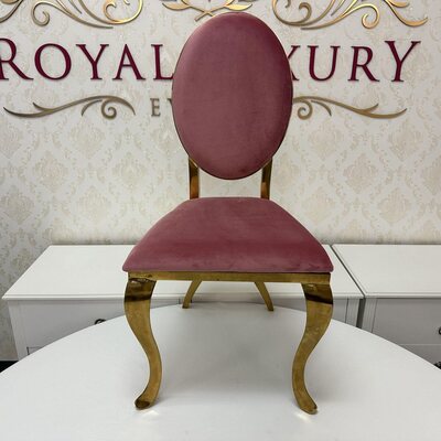 Pink velvet oval-back chair with curved gold legs, front view, set before a cream damask wall and white cabinets