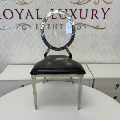 Showroom front view of silver dining chair with clear round back and black seat, white cabinets behind