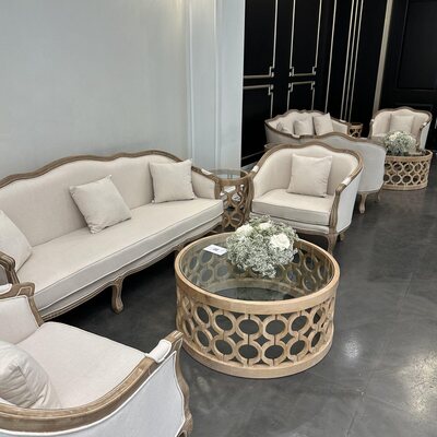 Row of off-white wood-framed lounge chairs and a sofa around a round table with white flowers, in a showroom