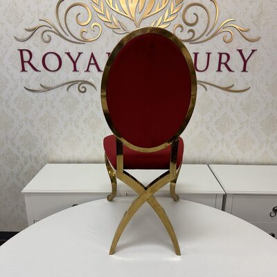 Rear view of ruby red oval chair back with gold frame and crossed gold legs, set before a white table
