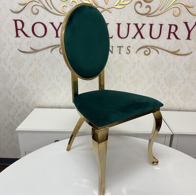 Gold cross leg chair with oval emerald green velvet back and seat, shown on a white table in a showroom