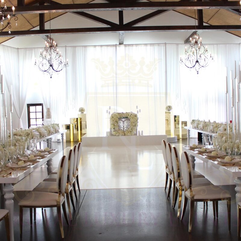 White fabric draping lining a rustic beamed venue, with long reception tables, tall white candles and gold-trimmed chairs