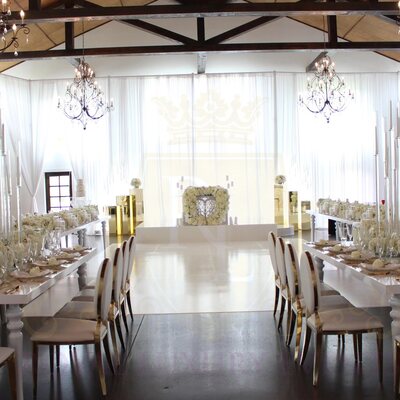 White fabric draping lining a rustic beamed venue, with long reception tables, tall white candles and gold-trimmed chairs