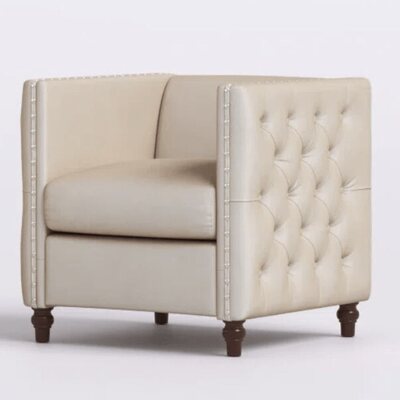 Beige tufted lounge chair with low back, nailhead trim and dark turned wooden legs, seen from the front corner