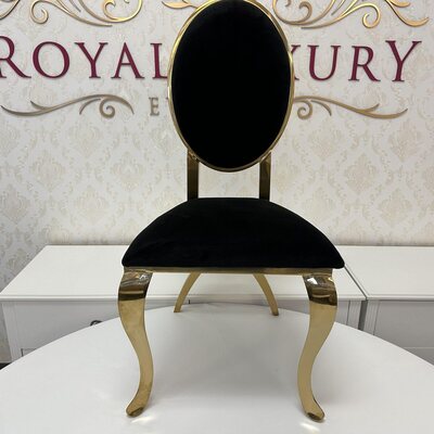 Front view of gold chair with oval black velvet back, set on a white table in the showroom