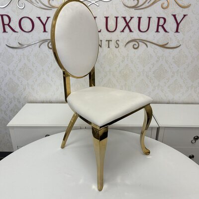 Gold chair with oval white velvet back, white velvet seat and curved polished gold legs, shown in a showroom