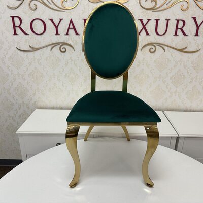 Front view of gold chair with emerald green velvet oval back and seat, set before a white cabinet