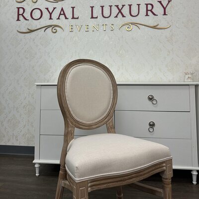 Wooden Louis chair with cream linen back and seat in front of a white dresser and gold lion crest sign