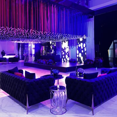 Black tufted velvet sofas facing each other across mirrored side tables beneath a hanging ribbon installation at a