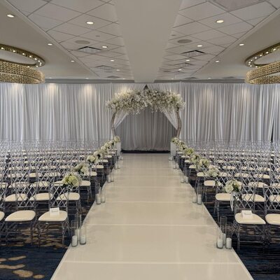 Rows of clear lattice-back chairs with white cushions lining an aisle at a ceremony in a ballroom