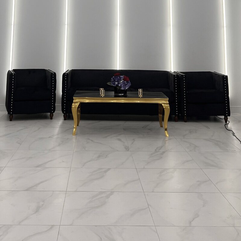 Black velvet three-seater sofa and two matching chairs with studded trim, set around a gold coffee table in a white room