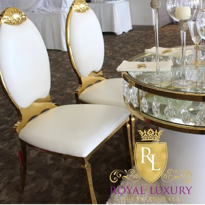 Gold chairs with white oval cushions beside a round mirrored sweetheart table with crystal drops, candles and white roses