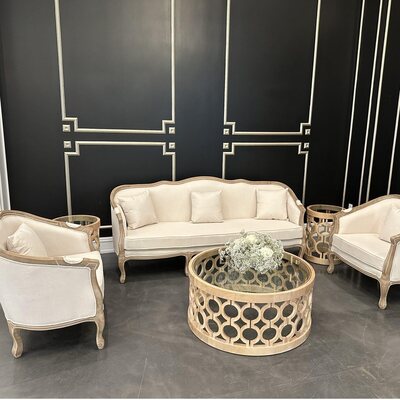 Off-white lounge chairs and sofa with wood frames around a round coffee table, set against a black panelled wall
