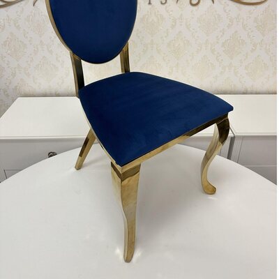 Gold chair with oval navy blue velvet back, matching seat cushion and curved polished legs, shown in a showroom