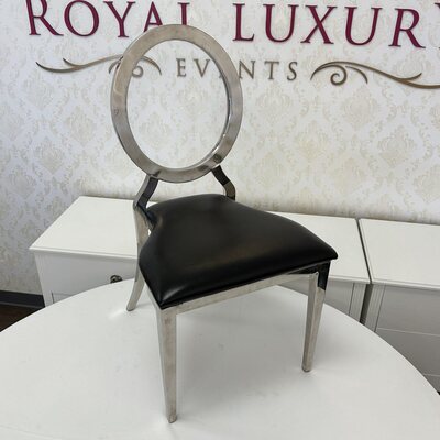 Silver round-back dining chair with black cushion on a white table, shown in the showroom beside white cabinets