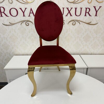 Front view of gold chair with ruby red velvet oval back and curved legs, set before a white table