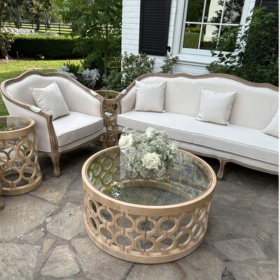 Off-white wood-framed sofa with cushions, beside matching armchair and glass-top lattice coffee table at Sandlewood Manor