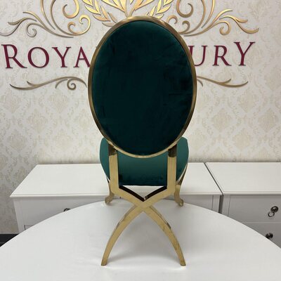 Rear view of gold chair showing emerald velvet oval back and crossed gold legs, set before a white cabinet
