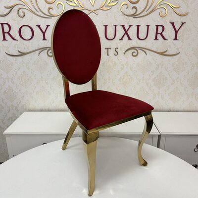 Gold chair with oval ruby red velvet back and seat, curved polished legs, shown on a white table in a showroom