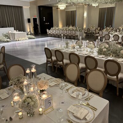 Wooden Louis chairs with oval cream backs at a draped reception table set with florals, candles and gold-rimmed plates