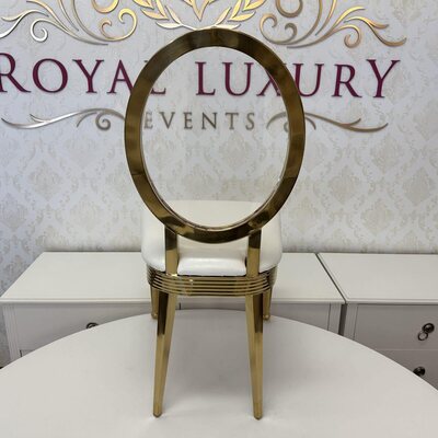 Rear view of a gold dining chair, showing the polished oval back frame and slim legs behind a white cushion
